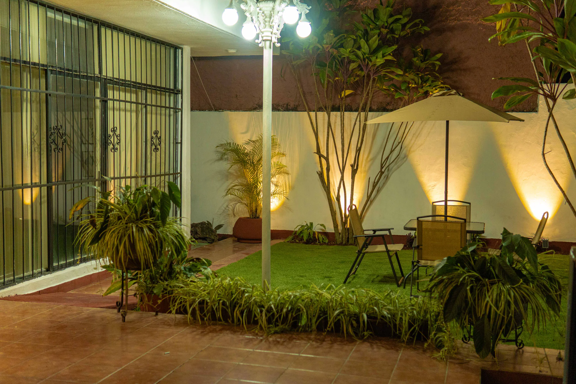 Patio interior de Los Olivos iluminado por la noche, con jardín, sombrilla y área de mesas